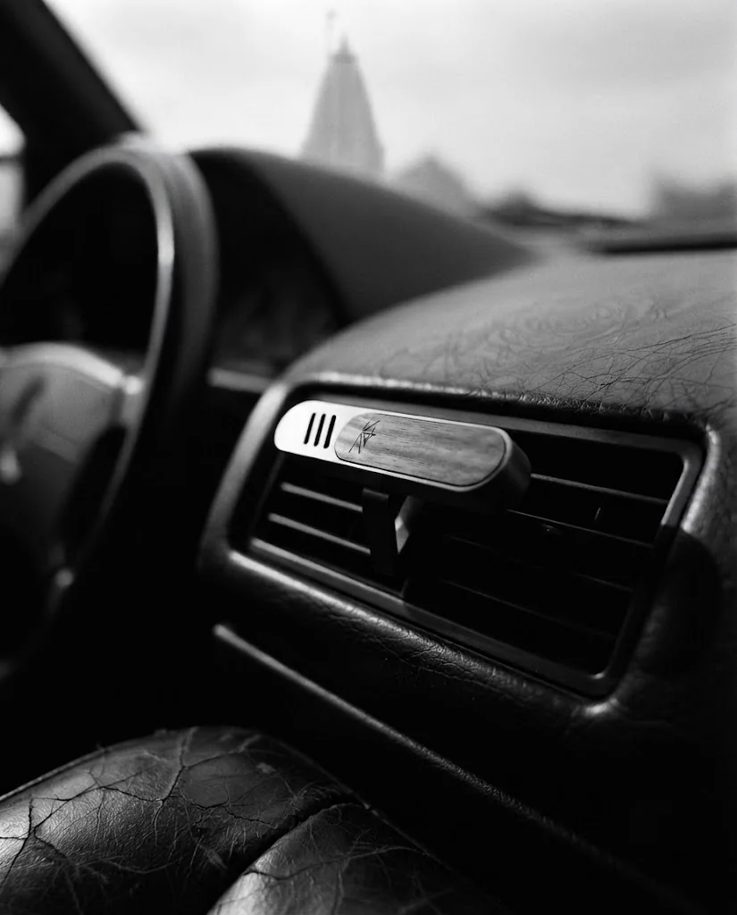 K4KAILASA vent-clip diffuser installed in a car air vent, dashboard and leather seat visible