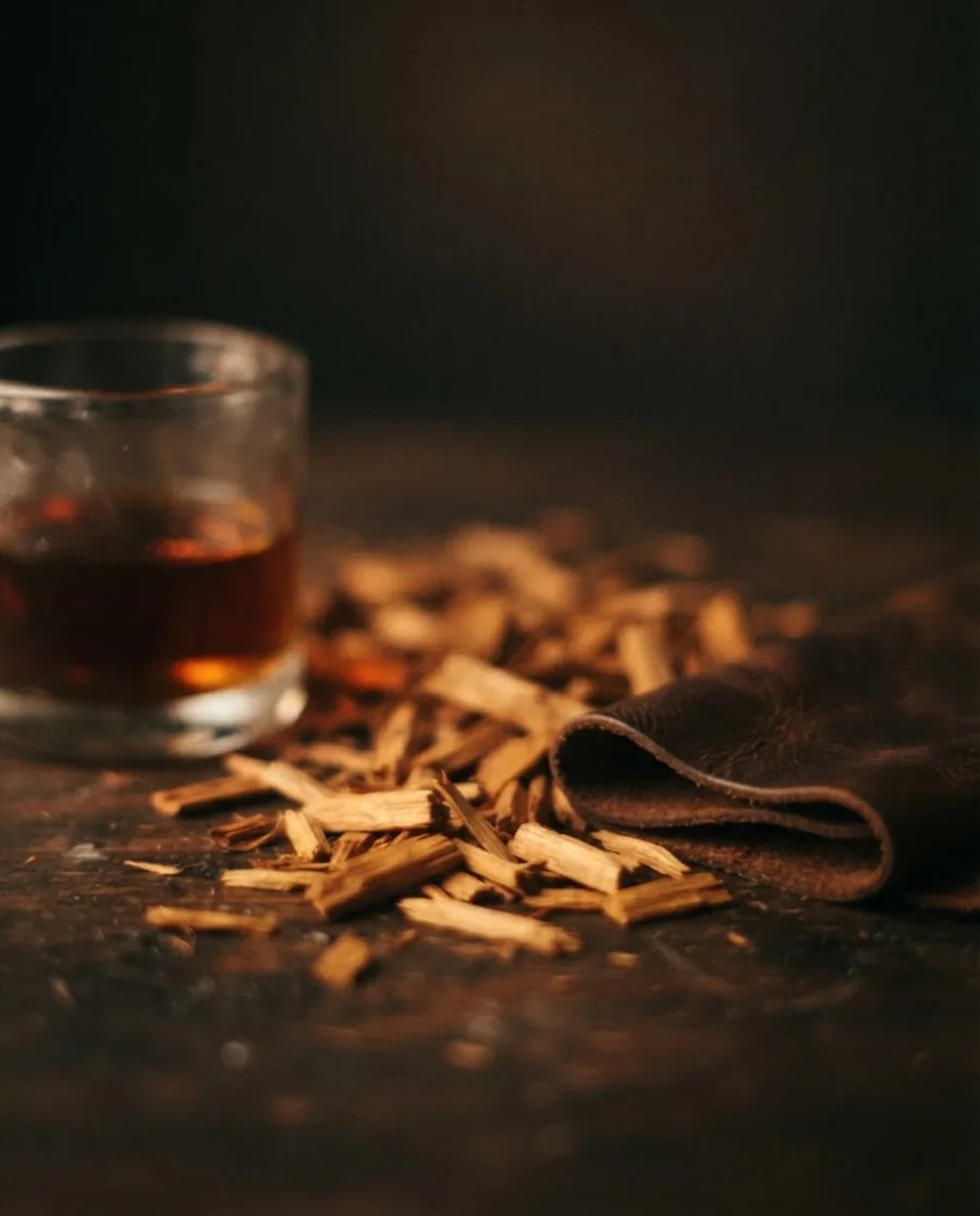 Sandalwood chips, leather, and amber liquid — VASANA fragrance still being formulated